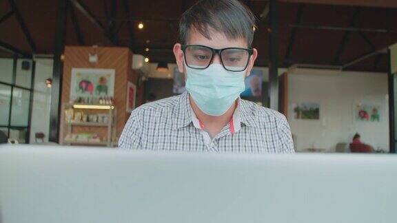 亚洲商人戴着口罩在咖啡馆里使用笔记本电脑工作