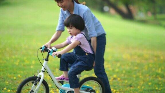 亚洲小女孩和年轻的老师在花园里骑自行车