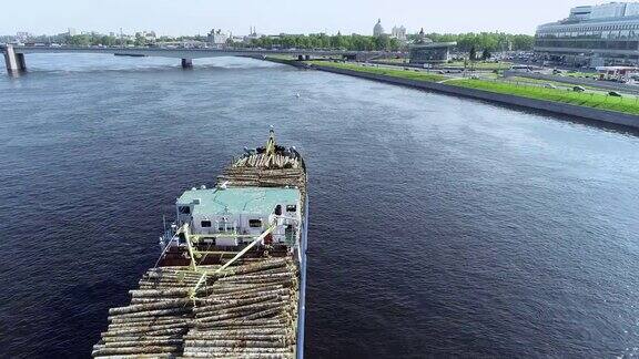 一艘载着木头的驳船载着桥从蓝色的大河上穿过城市