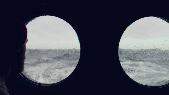 在波涛汹涌的海面上一名长胡子的水手站在一艘船的舷窗前