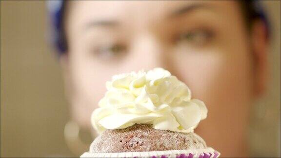 特写女人在纸杯蛋糕上浇上奶油和草莓