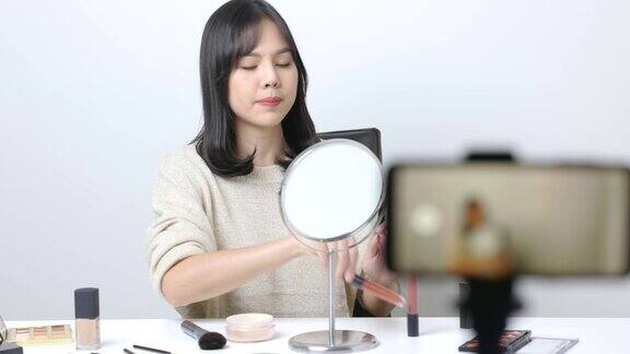 年轻的美丽博主亚洲女人用智能手机谈论使用粉和刷的化妆品网红化妆教人如何在社交媒体上化妆4k决议