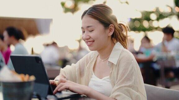 快乐的亚洲女性坐在海边的餐厅里使用电子平板电脑