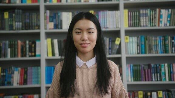 长头发的亚洲年轻女子站在图书馆微笑