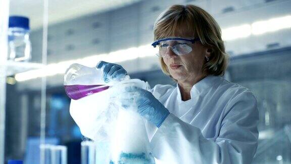 安全眼镜高级女化学家在烧杯中混合吸烟液体她在一家明亮的现代实验室工作