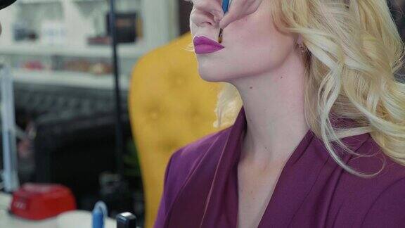年轻的化妆师在模特的嘴唇上涂口红