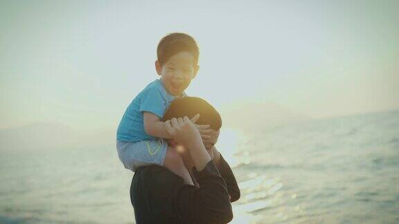 家庭旅游度假父亲抱着儿子在海滩上放松