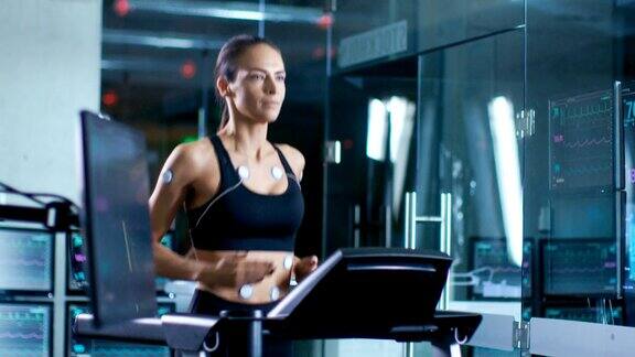 在科学运动实验室美丽的女人运动员在跑步机上跑步电极附在她的身体上显示器显示心电图数据缓慢的运动
