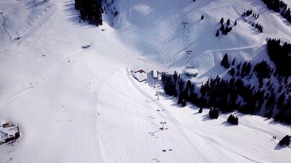 滑雪场天气晴朗树木繁茂的山的滑雪坡上的雪许多游客在滑雪缆车站和咖啡馆附近鸟瞰图