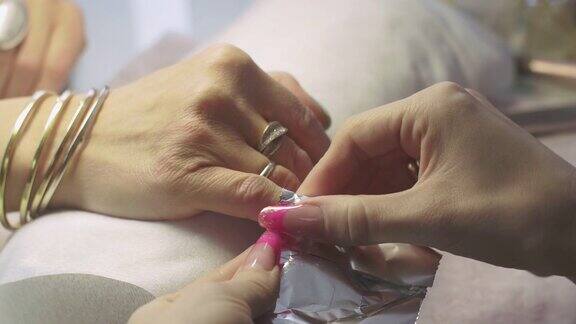 美容院的美甲师把棉垫和金属箔放在女人的指甲上指甲虫胶删除
