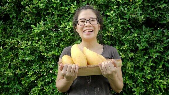 快乐的亚洲女人拿着一个木篮子芒果水果在户外
