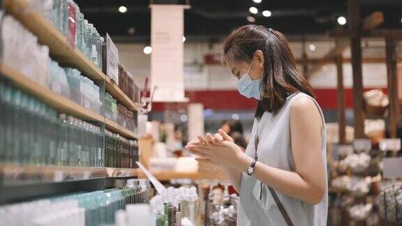 年轻的亚洲女性在商店购物时会戴口罩选择化妆品在试吃东西前后使用洗手液