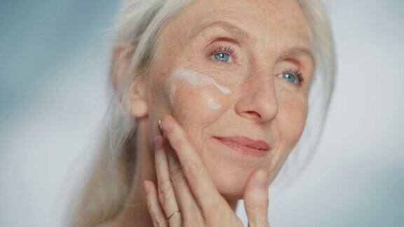 美丽的老年妇女肖像轻轻涂抹面霜使用天然抗老化化妆品使老妇人的皮肤柔软光滑无皱纹产品为美容护肤化妆