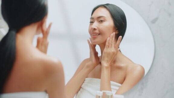 美丽的亚洲妇女肖像轻轻应用面霜在浴室镜子年轻女性使她的皮肤柔软光滑无皱纹的天然抗衰老化妆品护肤品