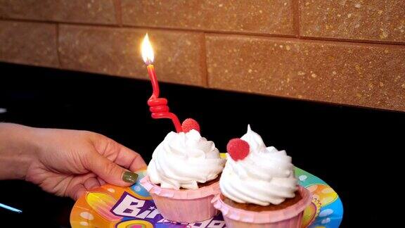 特写在一个节日盘子上有两个漂亮的白色奶油和浆果纸杯蛋糕一根蜡烛在一个纸杯蛋糕上燃烧着生日蛋糕