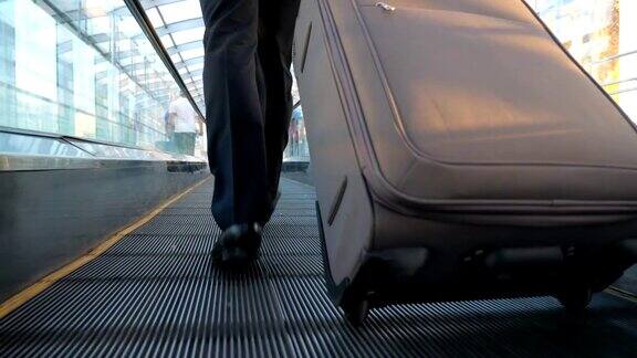 成功商人的脚和行李走在航站楼的大厅富商的双腿行走在自动扶梯上拖着带轮子的手提箱出差慢镜头