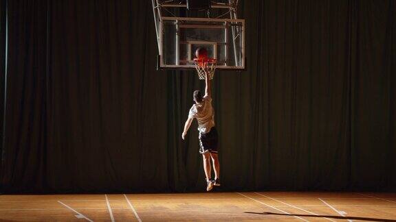 年轻的白人篮球运动员打球把球投进篮筐胜利者晚上在体育馆的拼花地板上运球
