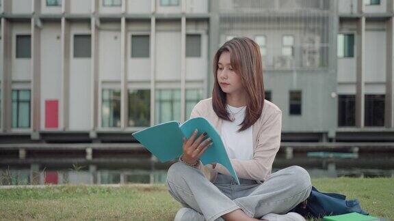 亚洲女子大学的学生坐在校园草地上看快乐和在公园看书