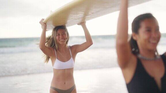 4K亚洲女性朋友拿着冲浪板一起走在热带海滩在夏日日落