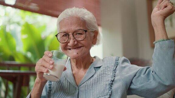 有魅力的亚洲老年人在闲暇时间在家喝一杯牛奶老妇人早上喝新鲜牛奶保健老年人健康的生活方式