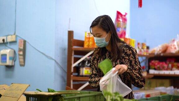 年轻的亚洲妇女戴着防护口罩在市场购买新鲜蔬菜