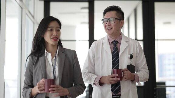 亚裔华人医生与女医药销售代表在医院走廊上同行