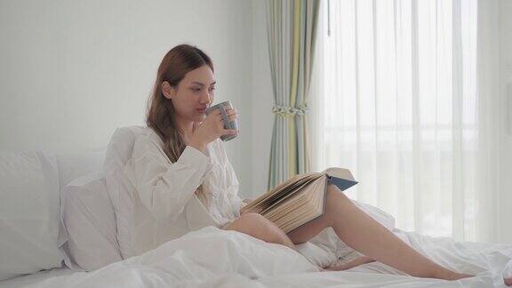 年轻女子早上坐在床上一边喝咖啡一边看书