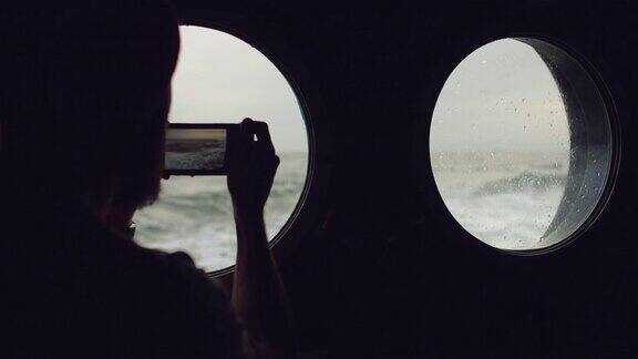在波涛汹涌的海面上一个人在一艘船的舷窗旁