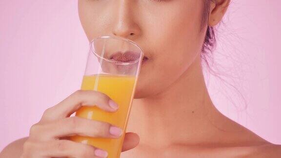 年轻快乐的女人喝橙汁在粉红色的背景清洁平衡的健康食品理念健康饮食与健身理念有机食品医疗保健理念视频:多样化的肖像