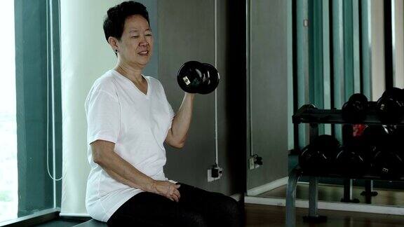 亚洲资深女子举着哑铃在健身室进行健康锻炼