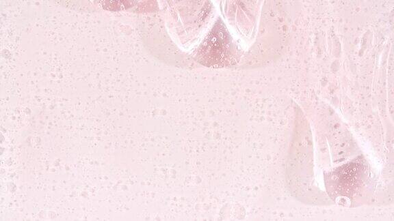 粉色透明化妆品凝胶液与分子气泡流动在平坦的白色表面微距镜头
