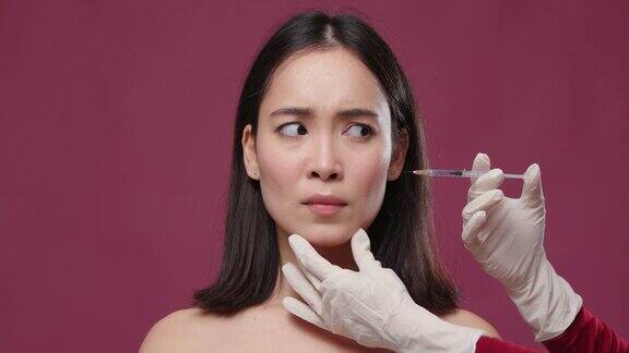年轻的亚洲女人害怕戴手套的医生试图给她脸上注射玛萨拉copyspace