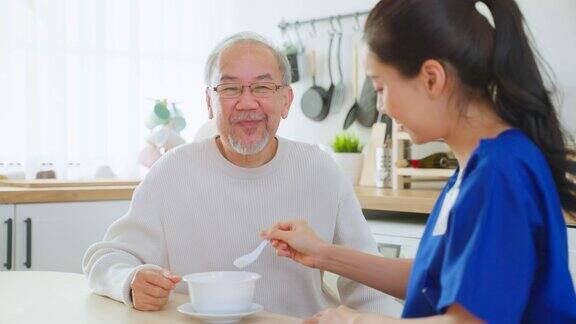 亚洲护理护士为坐在餐桌上的老人提供食物迷人的年轻专家护理员女医生支持和照顾快乐的老人成熟的爷爷在养老院