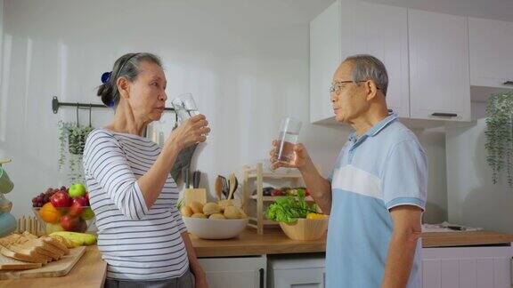 亚洲老年夫妇在家里的厨房里喝一杯水成熟的年长的口渴的祖父母抱着清洁的天然矿物在杯子醒来后在早上的健康护理在家里啜饮