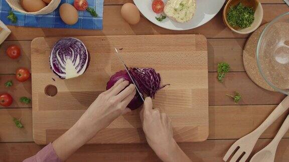 年轻的亚洲女厨师手握刀把红白菜切在家里的餐桌木板上