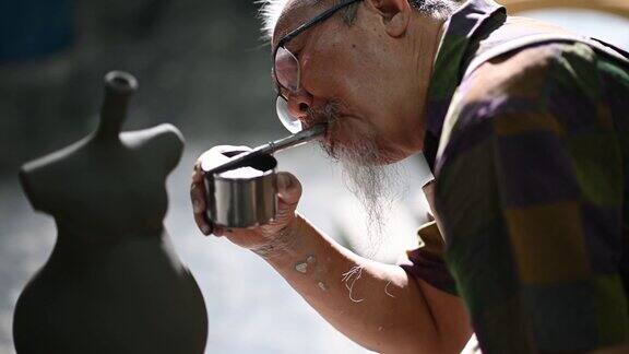 亚洲华人高级泥塑艺术家在雕塑家身上吹颜料在他的工作室里用纺纱陶轮工作