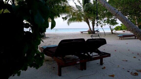 热带海滩上的一棵棕榈树下的木制躺椅马尔代夫