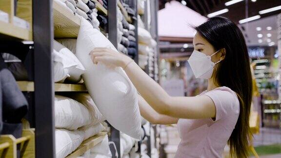一位亚洲妇女戴着防护口罩在一家零售店里挑选枕头