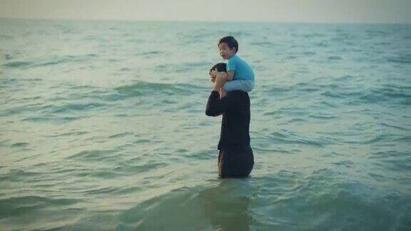 家庭旅游度假父亲抱着儿子在海滩上放松