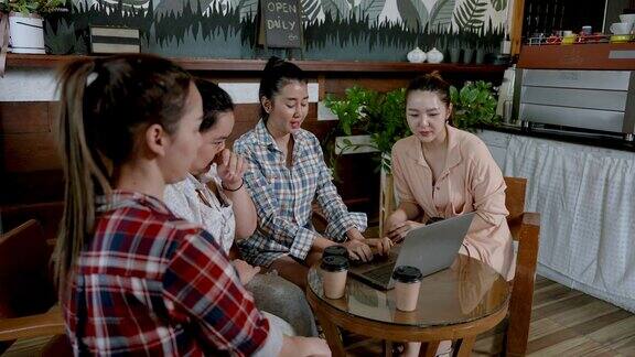 一群亚洲女同事在咖啡馆的一张桌子上愉快地聊天喝着美味的饮料在白天使用笔记本电脑在咖啡店上网工作之前