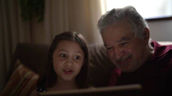 祖父和孙女正在用家里的平板电脑进行视频通话