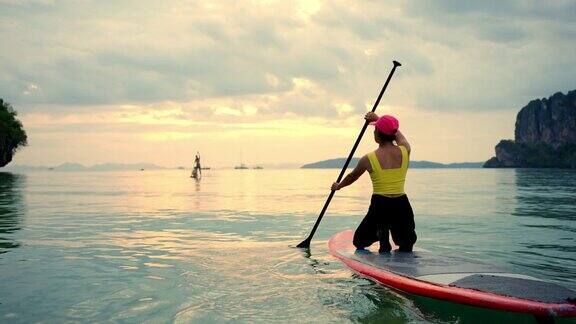 4K亚洲成熟女子坐在桨板上划船在热带岛屿日落