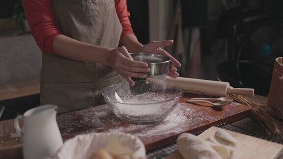 面包师在传统面包房的餐桌上用筛子筛面粉
