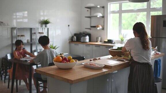 两个孩子在家学习写中国书法而他们的母亲在厨房柜台准备食物