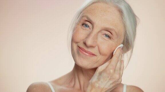 中等画像:美丽的老年妇女用棉花垫清洁她完美的脸上的化妆品微笑的老妇人与柔软的皮肤优雅的老年及天然护肤洁面产品