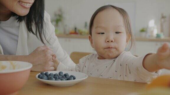 可爱的小女孩吃着浆果妈妈在厨房里和孩子说话亲吻着表达爱