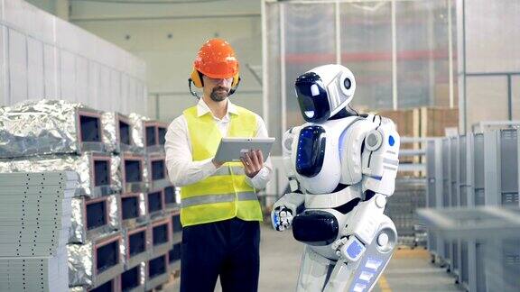 一名男性工厂员工正在向一个机器人解释一些事情并调节它的设置
