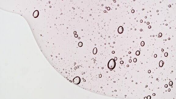 粉色透明化妆品凝胶液与分子气泡流动在平坦的白色表面微距镜头