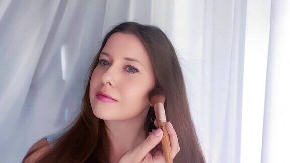 美丽的年轻女子使用化妆刷化妆粉慢动作肖像室内美妆和护肤化妆品