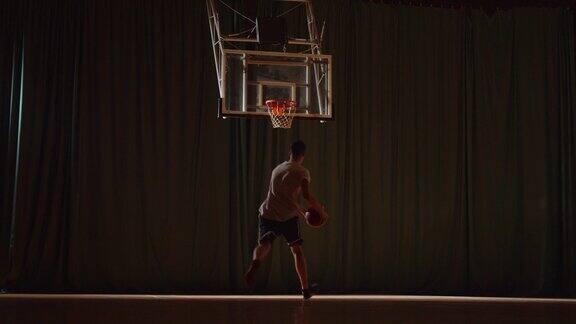 年轻的白人篮球运动员打球把球投进篮筐夜场体育馆拼花地板运球光束